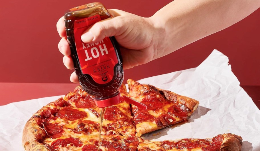 hand squeezing Nature Nate’s Hot Honey over a pizza