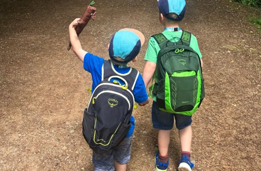 kids wearing navy blue and green osprey backpacks on dirt road