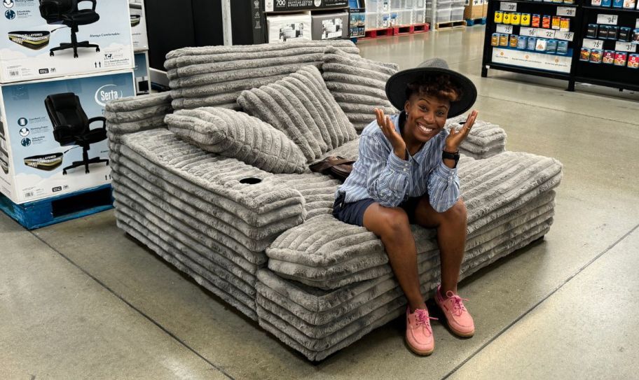 a woman sitting on an oversized gray chair in a sams club