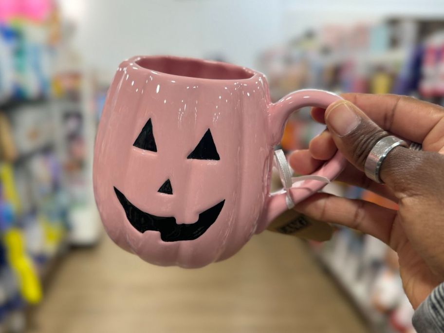 womans hand holding a pink jack o'lantern coffee much