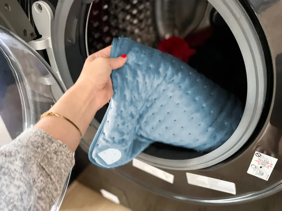 person putting a heating pad into a front loading washing machine