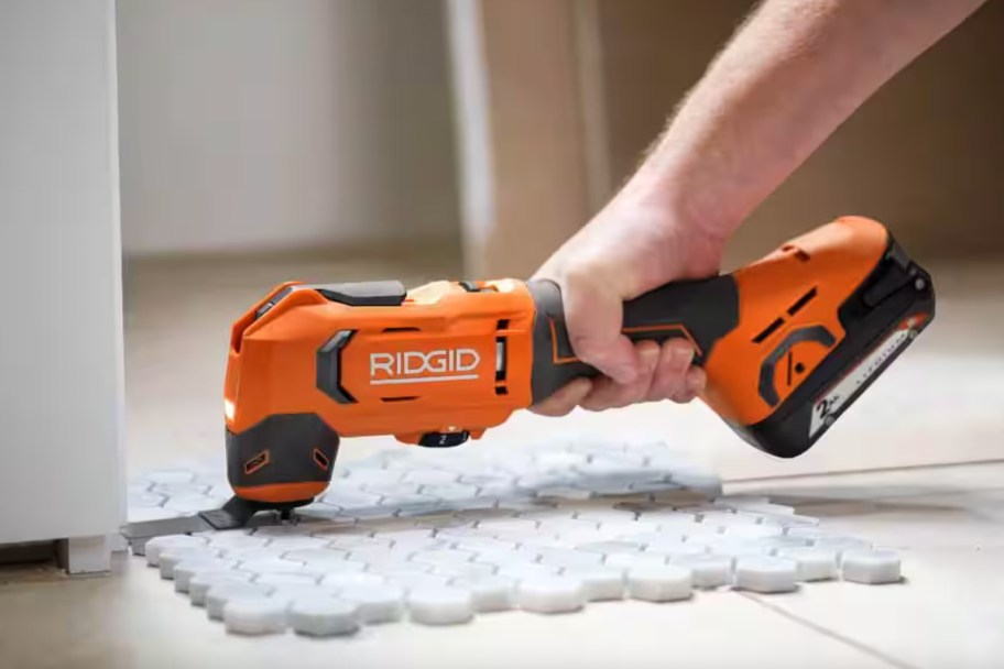 hand using orange multi tool on floor