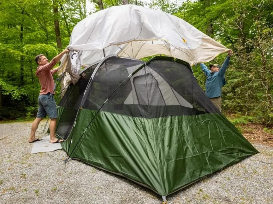 2 men putting the top on a large green and tan dome tent