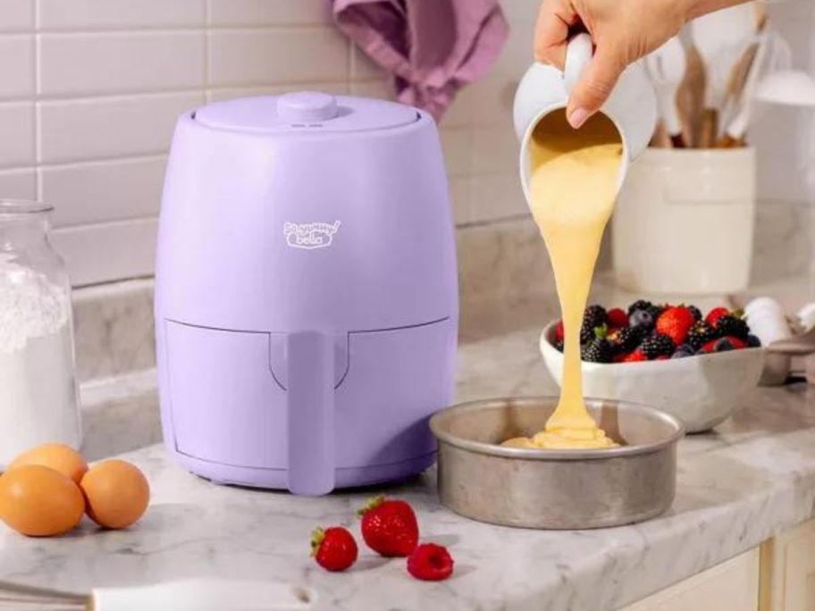 So Yummy by bella 2-Quart Air Fryer on counter next to hand puring cake mix into cake pan