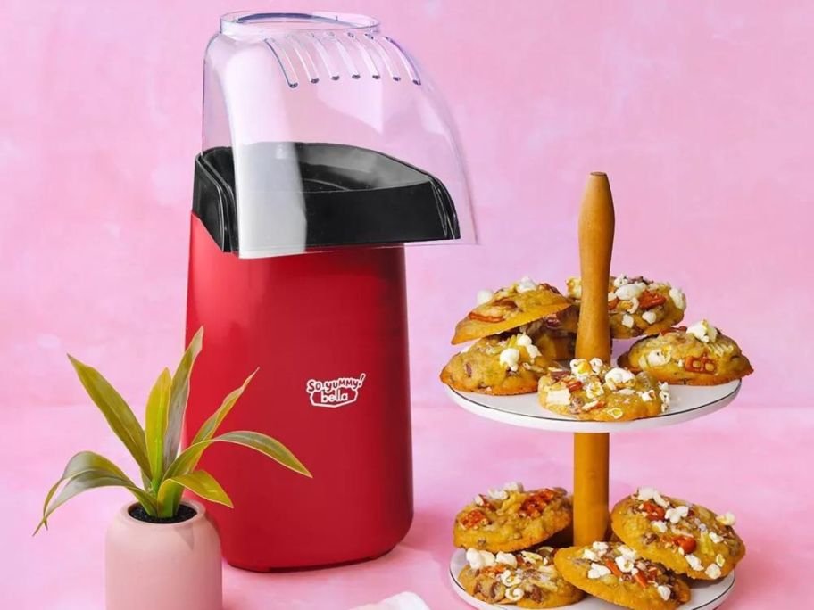 So Yummy by bella 16-Cup Popcorn Maker on counter next to a cookie stand and plant