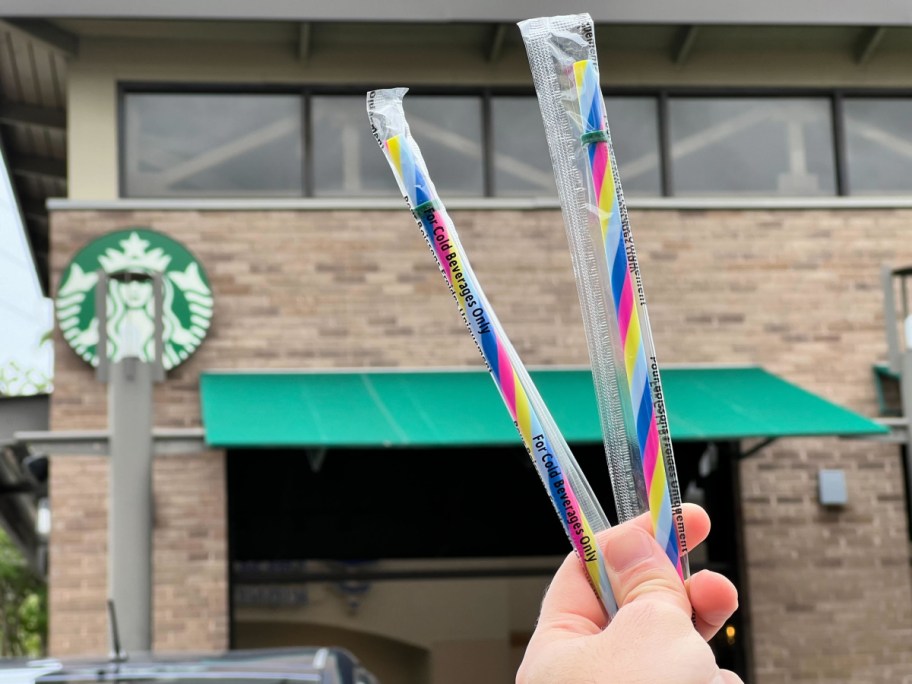 wman holding up colorful reusable straws in front of a starbucks
