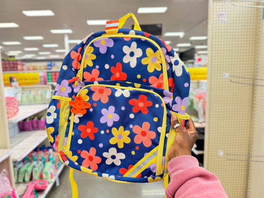 hand holding a kid's backpack in a bluish purple with daisies