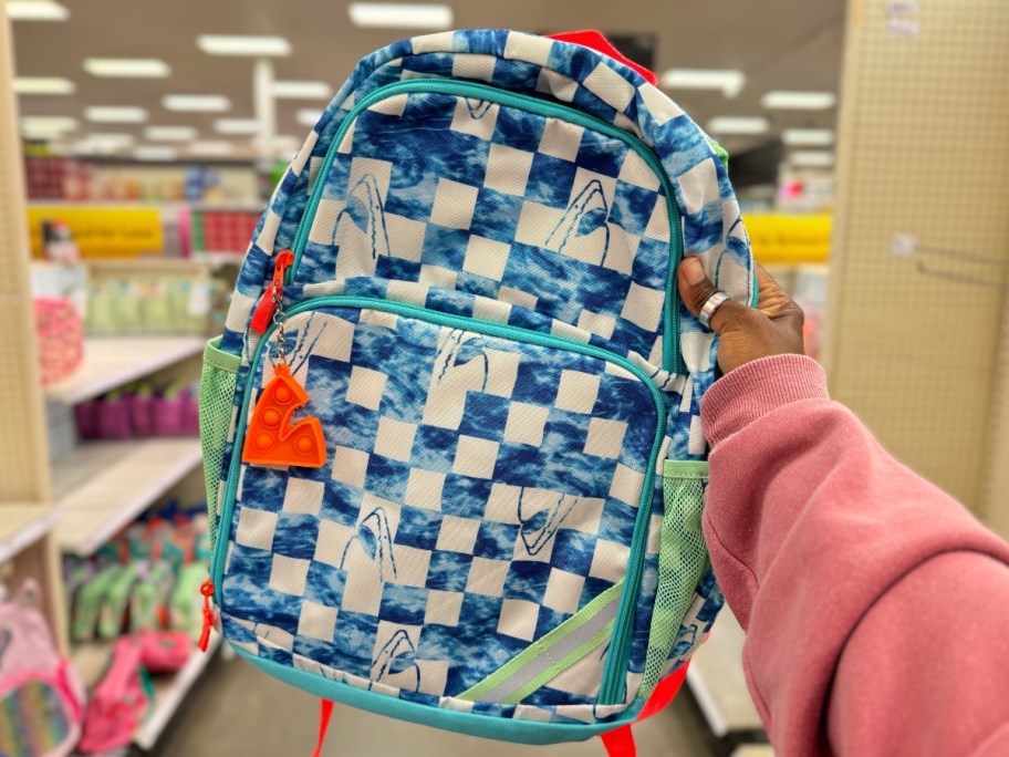 hand holding a kids' backpack in blue and white checkers with sharks on it