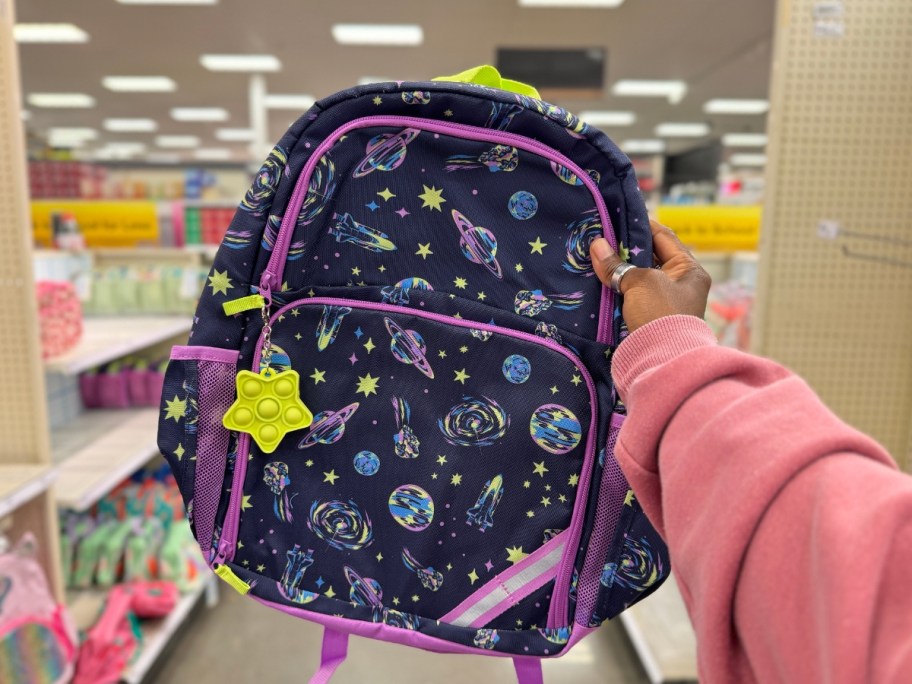 hand holding a kid's blue backpack with space items on it