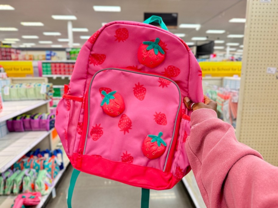 hand holding a kid's pink backpack with strawberries on it