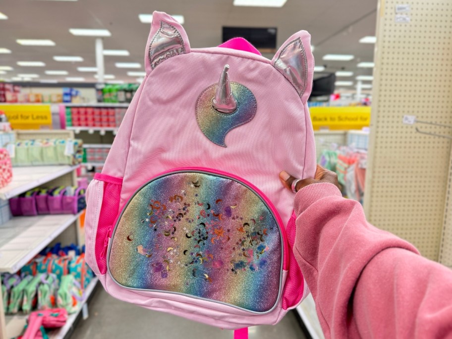 hand holding a kid's pink and iridescent unicorn backpack