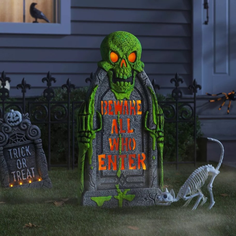 large Halloween decor lit up tombstone with a skull that says "Beware All Who Enter"