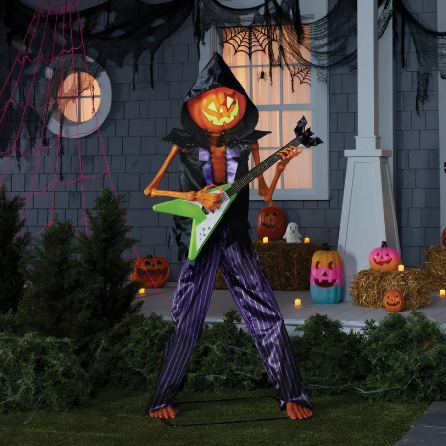 large pumpkin head ghoul Halloween decoration dressed like a rocker with a guitar outside a house