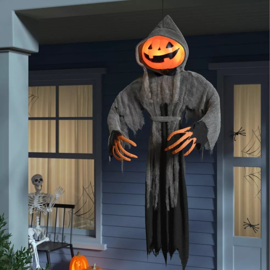 Halloween pumpkin head skeleton ghoul wearing a grey and black robe hanging on a front porch