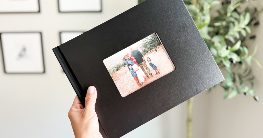 hand holding a black photo book with a window on the cover showing a family picture