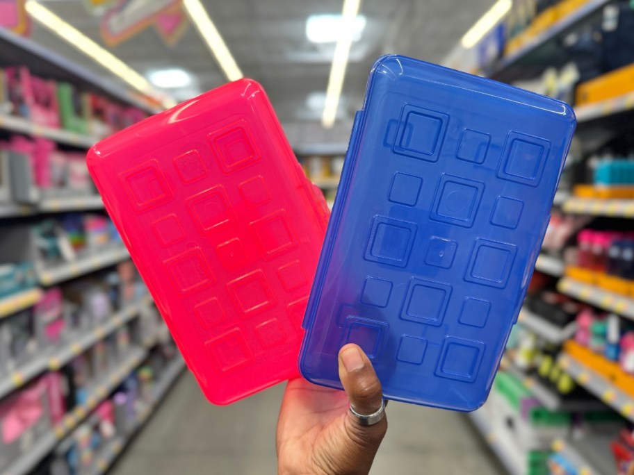 hand holding a red and a blue plastic pencil case in a store aisle