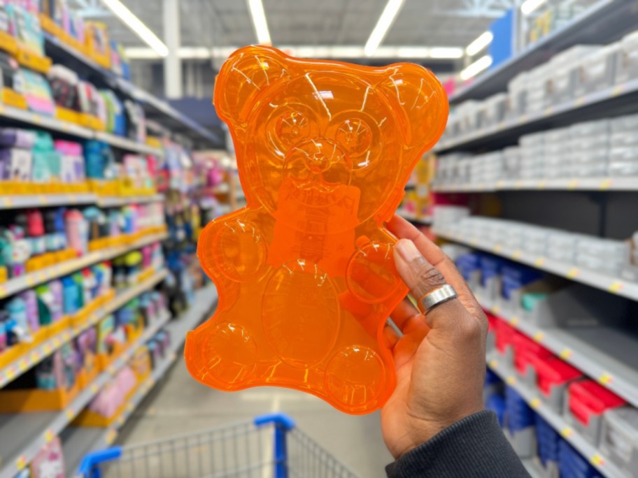 hand holding an orange gummy bear shaped plastic pencil case in a store aisle