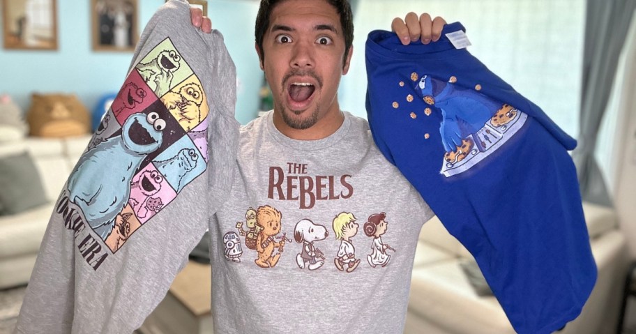 man wearing a Peanuts graphic tee, holding a cookie monster and sesame street tee in each hand