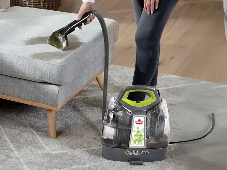 person using a Bissell Little Green Pet Cleaner tool to clean a stain off the end of a chaise sofa