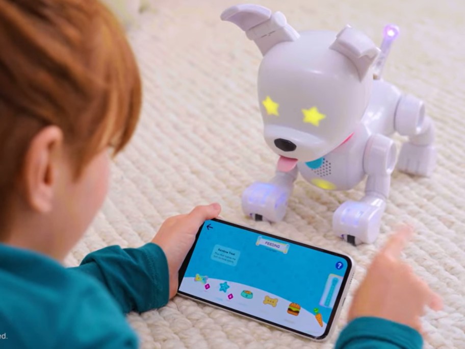 kid using an app on a smart phone to play with a white robot dog