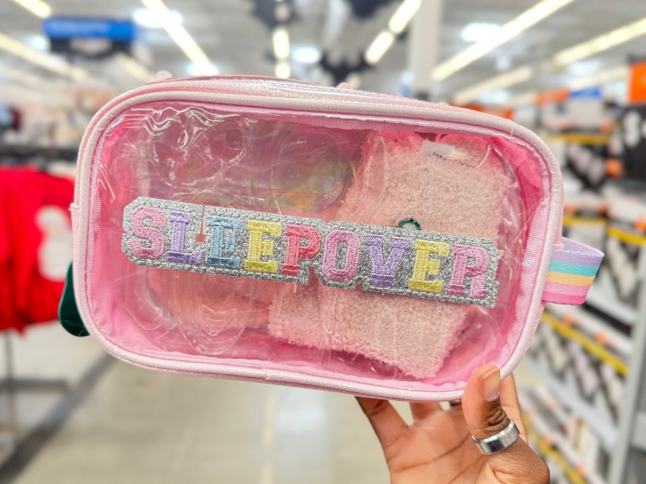 hand holding a clear and light pink zip accessory bag with travel accessory items in it that says 