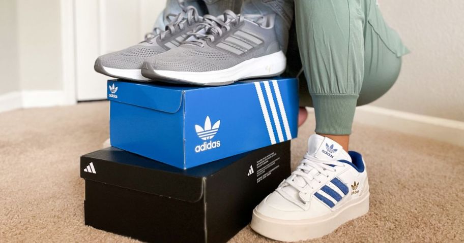 Boxes of Adidas Shoes with a woman wearing adidas shoes crouching next to them