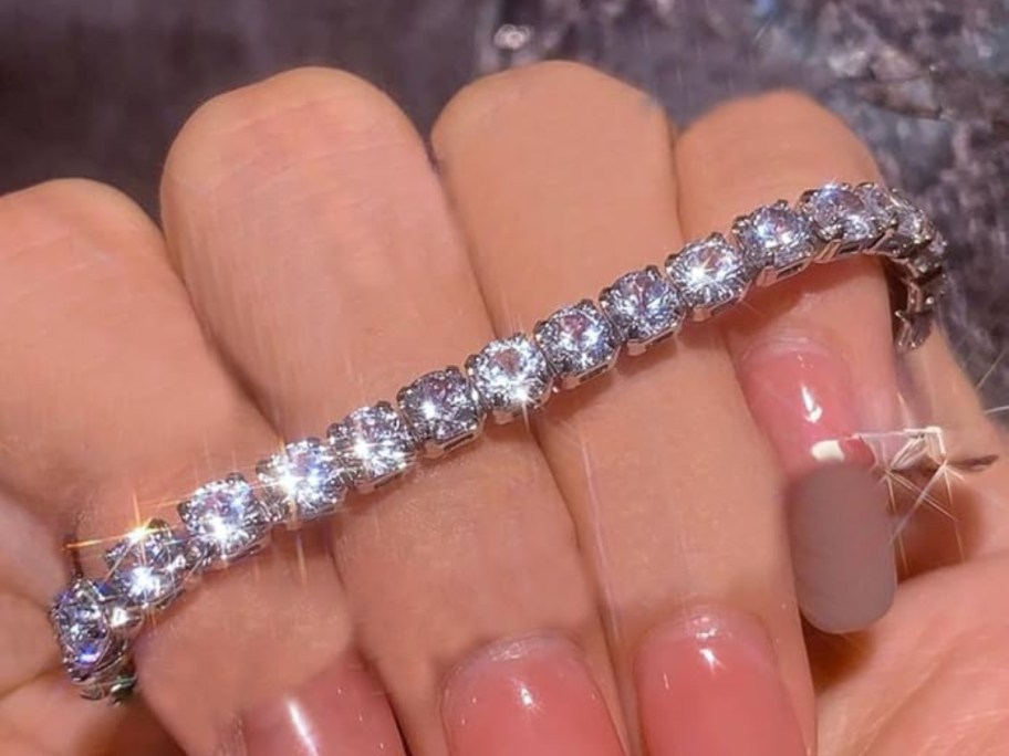 woman's hand with pink fingernails holding a silver diamond tennis bracelet