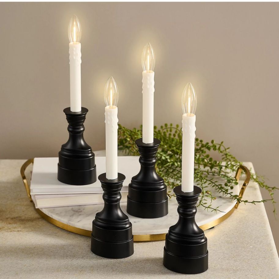 four Cordless Window Candles with black matte colored bases on a tray with evergreen sprigs 