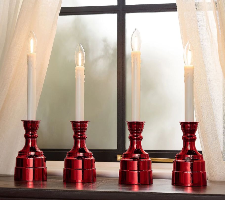 four Cordless Window Candles with red metallic bases in a window