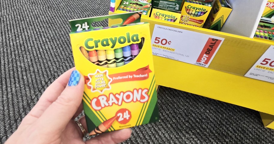 hand holding up a pack of crayola crayons in front of sale sign