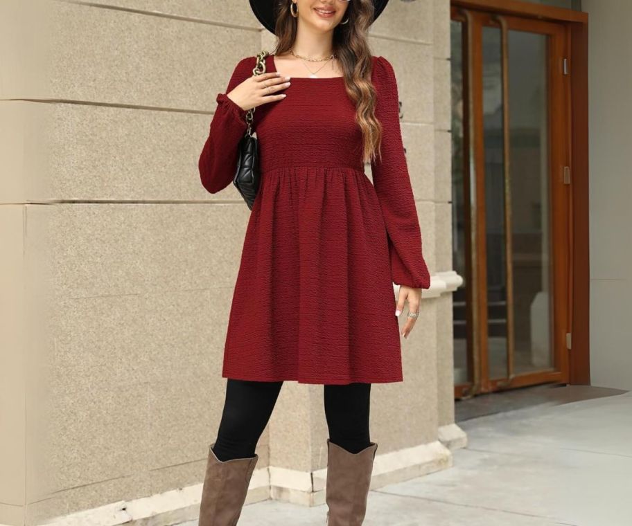 a woman in a burgundy mini swing dress in front of a building standing n a sidewalk