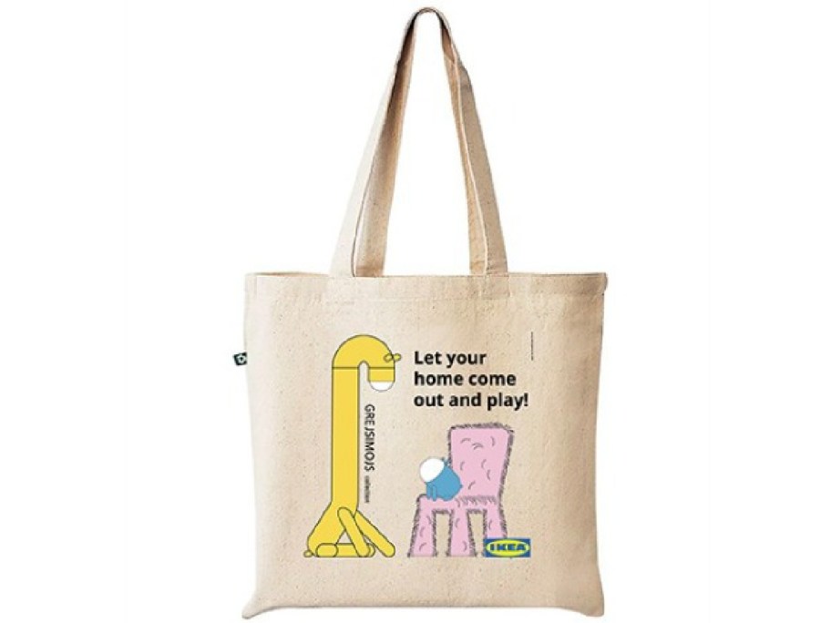 Canvas tote bag featuring a whimsical illustration of a yellow creature and a pink furry chair playing with a ball. Text reads, "Let your home come out and play!"