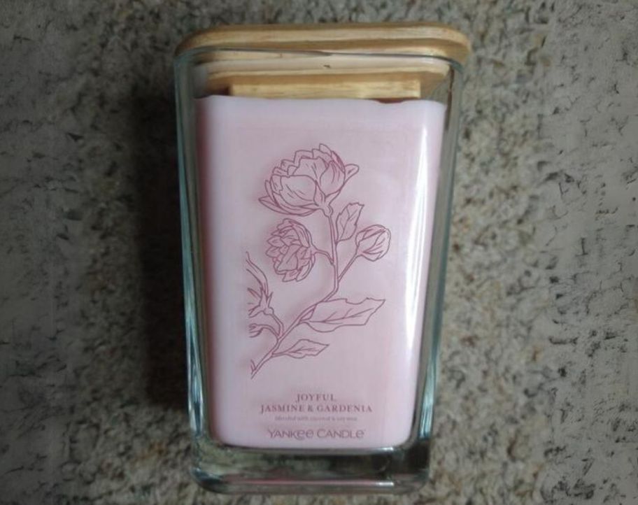 a large pink candle in a square glass jar laying on its side on a counter top