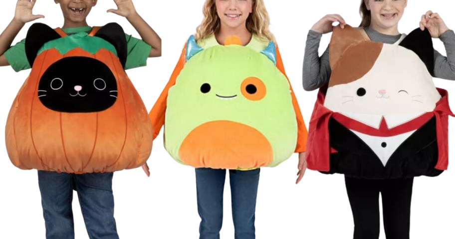 kids wearing Squishmallow Halloween Costumers, one is a pumpkin black cat, one is a monster, and one is vampire cat