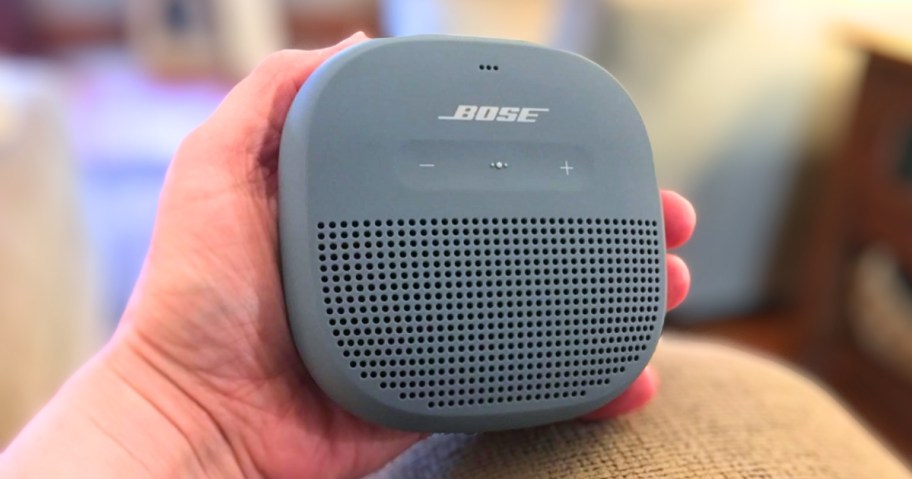 a hand holding a small Bose Bluetooth wireless speaker