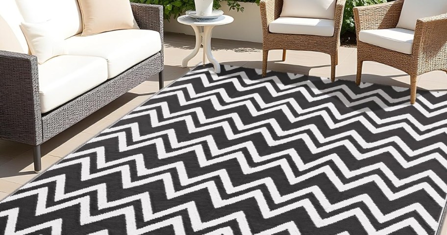 a black and white chevron outdoor rug on a back patio area with 2 outdoor chairs and a loveseat and table 