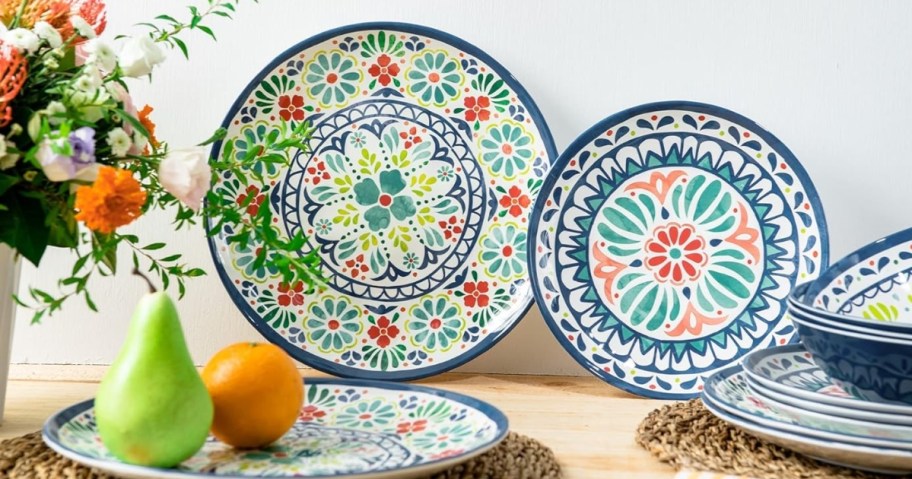 a colorful medallion print dinnerware set on a counter with fruit