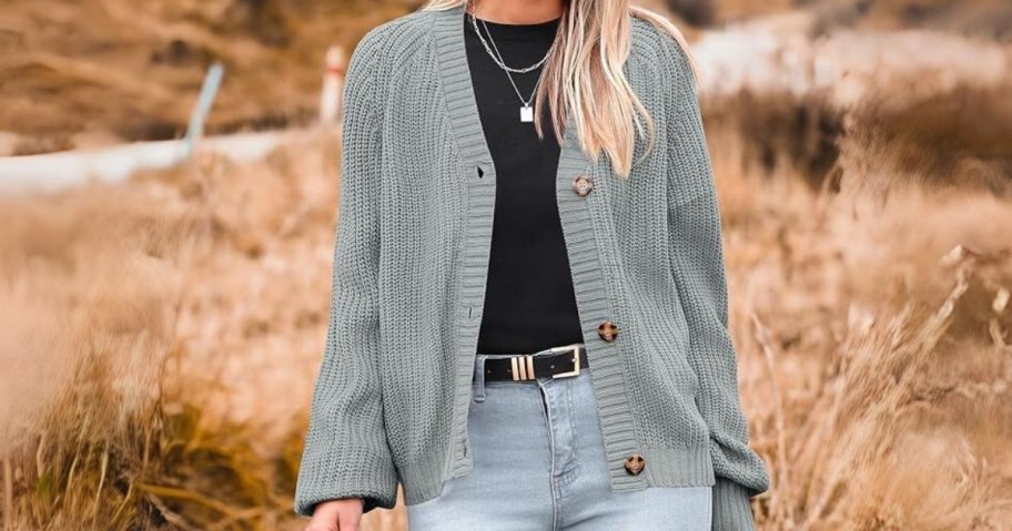 woman wearing a grey cable knit button up sweater with a black shirt and jeans, standing outside