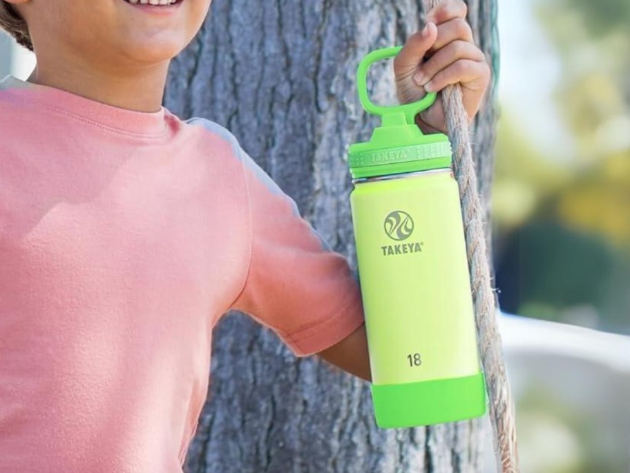 little boy on a rope swing hanging on a tree holding a bright green and yellow water bottle