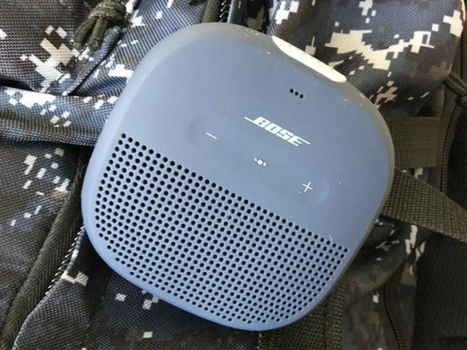 a small blue Bose wireless Bluetooth speaker on a black and white backpack