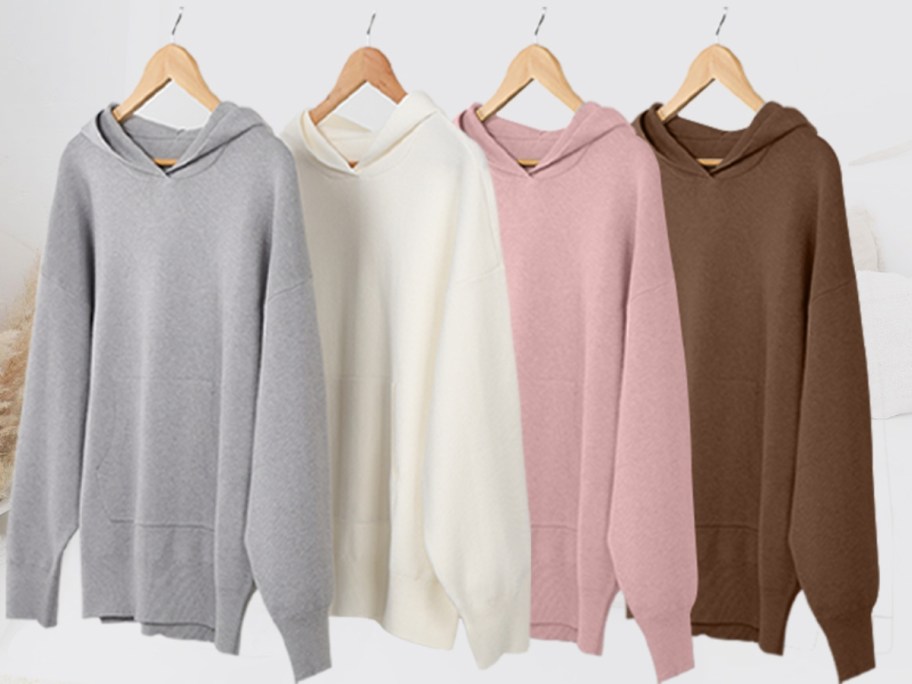 grey, white, pink, and brown knit hoodies on wood hangers on a rack