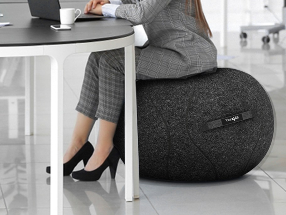 woman wearing a grey pants suit sitting at a desk on a black yoga ball seat