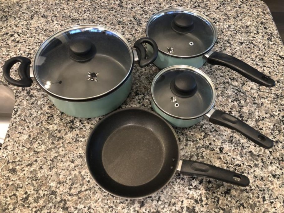 sage green and black cookware set with 3 pots with lids and a frying pan on a kitchen counter