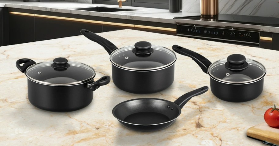 black cookware set with 3 pots with lids and a frying pan on a kitchen counter