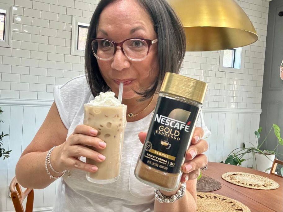 A woman holding a NESCAFÉ Gold Espresso Blonde Instant coffee canister while she is drinking a yummy-looking iced coffee