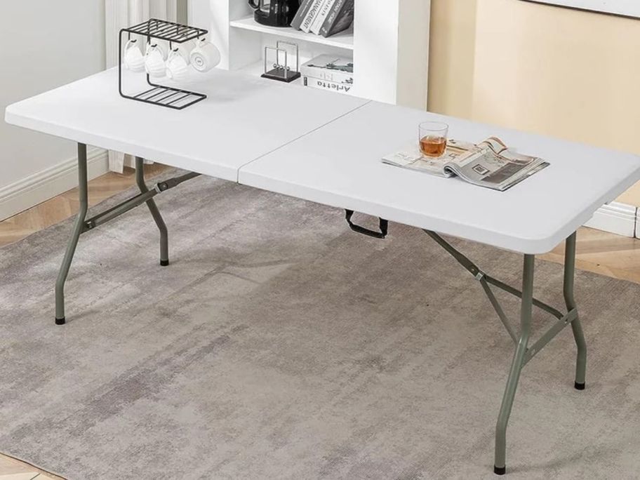 A plastic folding table with a rack of coffee cups, a magazine and a glass on it
