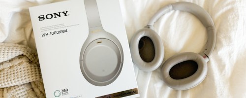 pair of silver Sony headphones on a bed next to the box they come in