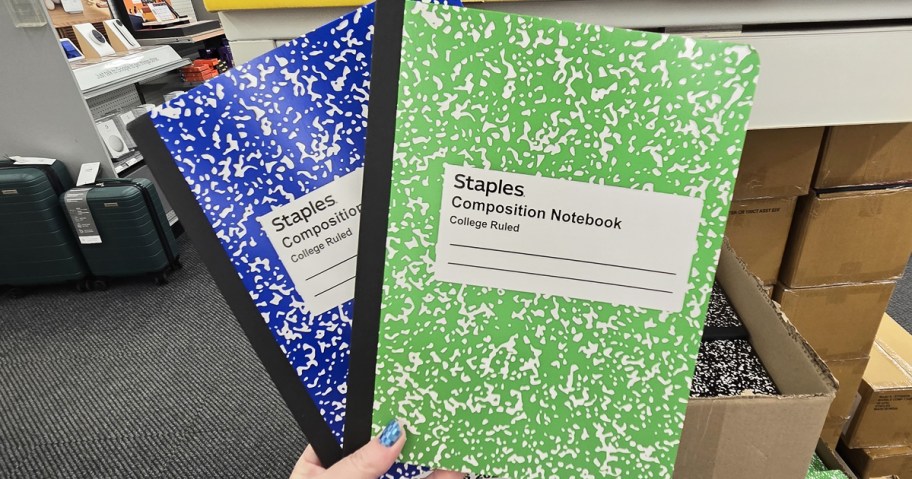 hand holding up green and blue Staples Composition Notebooks