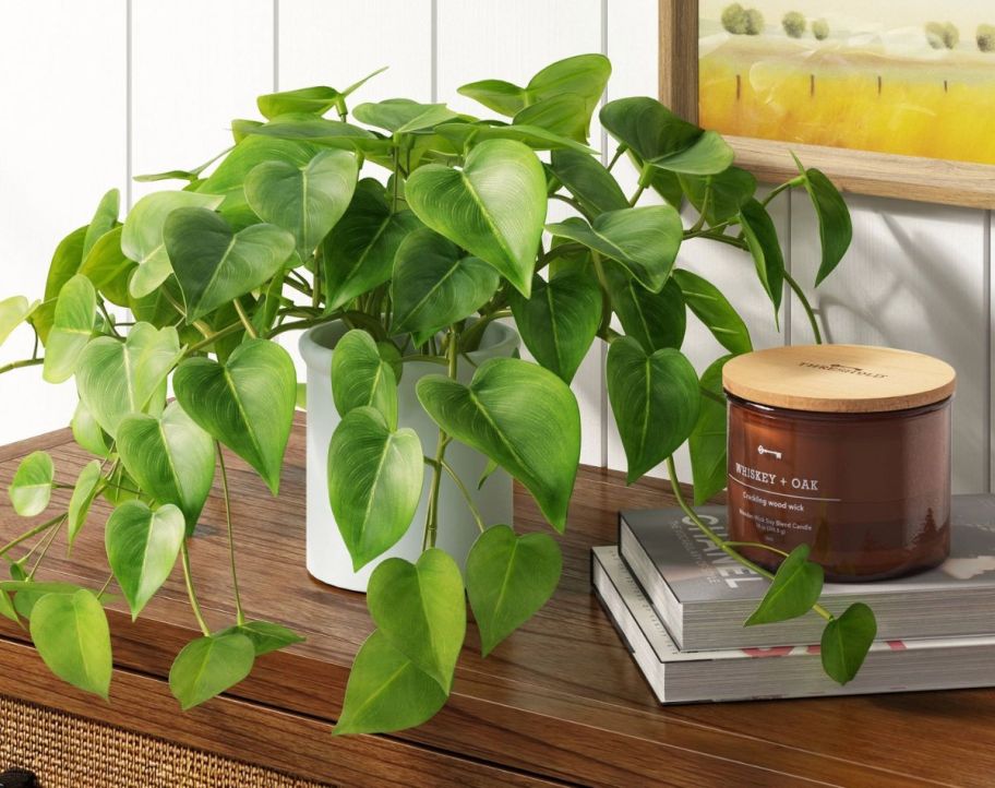 a large leafy faux plant on a table next to a candle