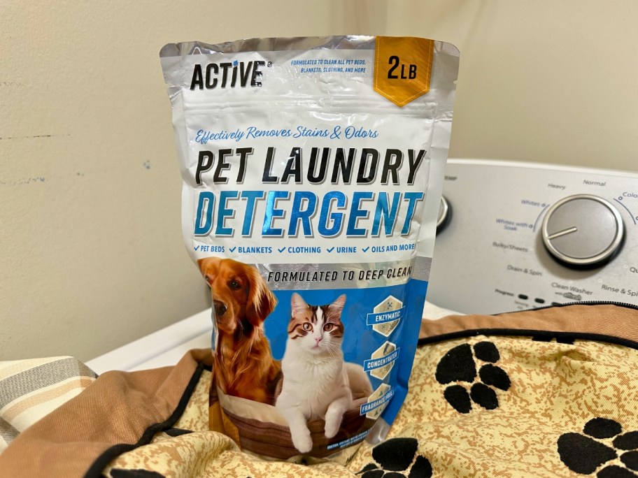 bag of Active Pet Laundry Detergent sitting on top of a tan and black dog blanket on top of a washing machine